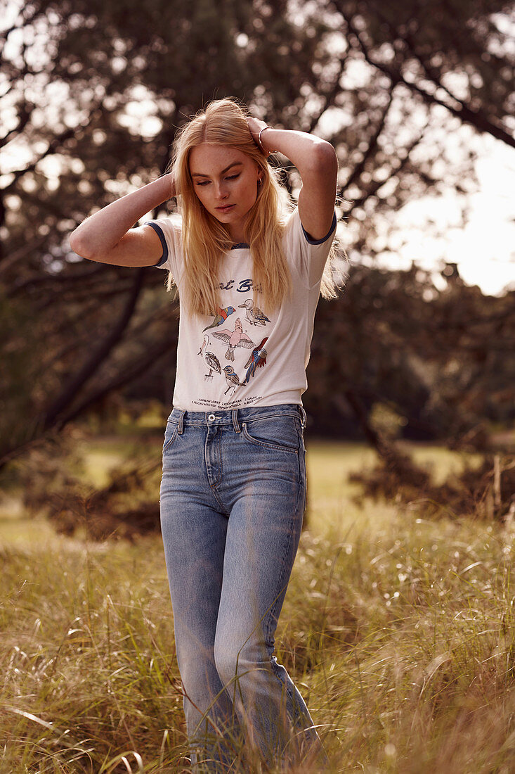 A young blonde woman wearing jeans and a T-shirt outside a field