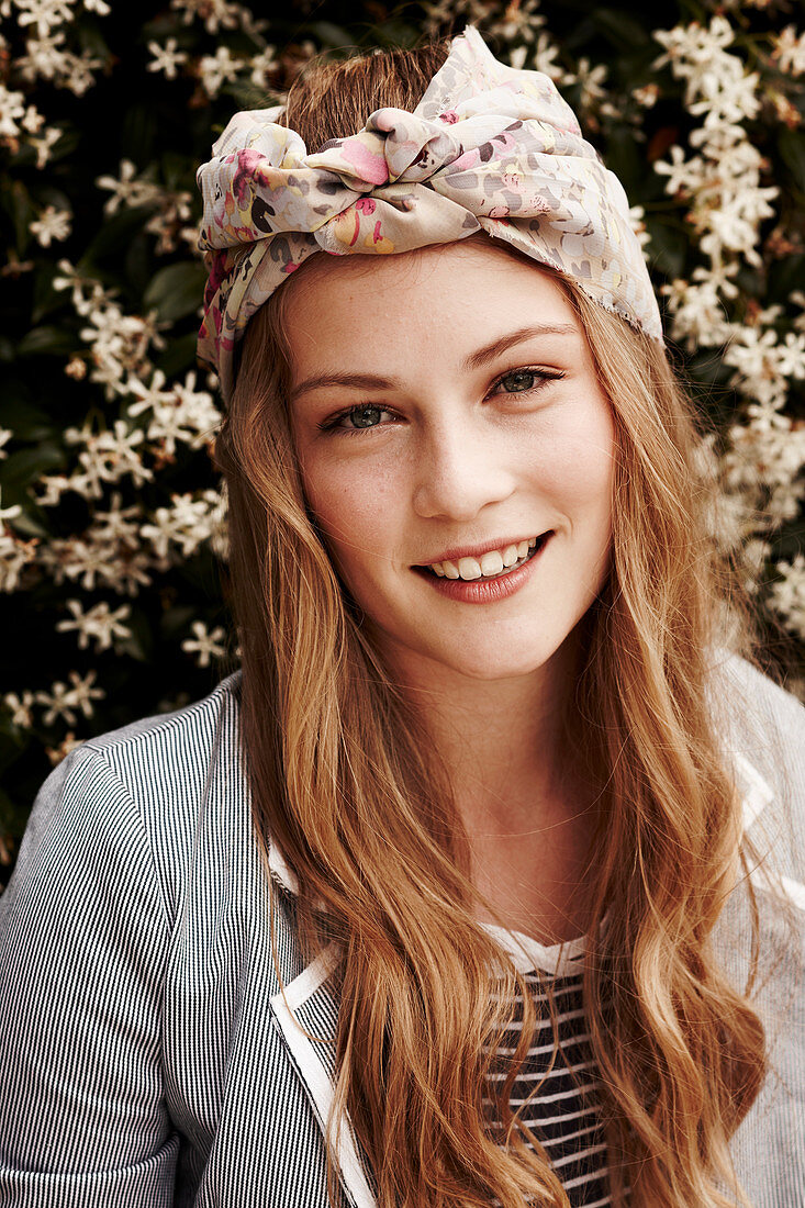 A young woman wearing a hairband standing in front of a flowering bush
