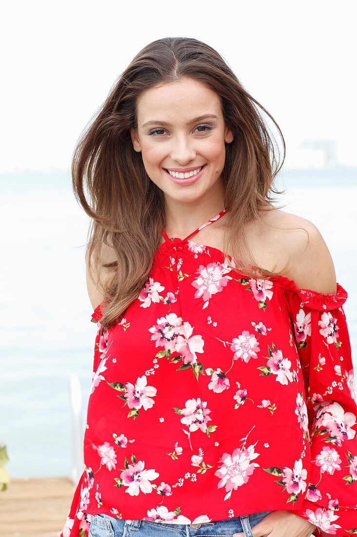 A brunette woman wearing a red Carmen blouse with a floral pattern