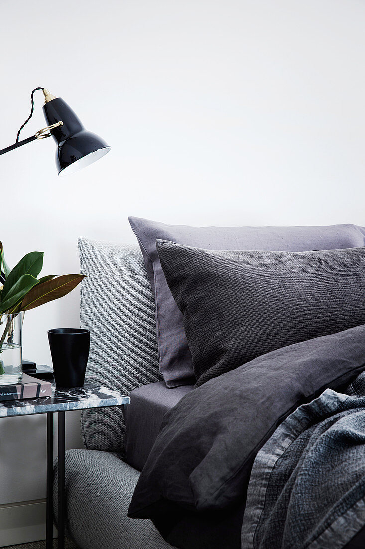 Bed with dark sheets, next to it marble bedside table