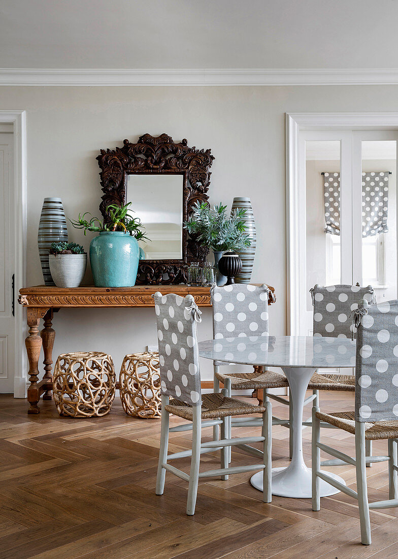 Chairs with polka-dot backrests at round dining table in front of wood-framed mirror and potted plants on console table