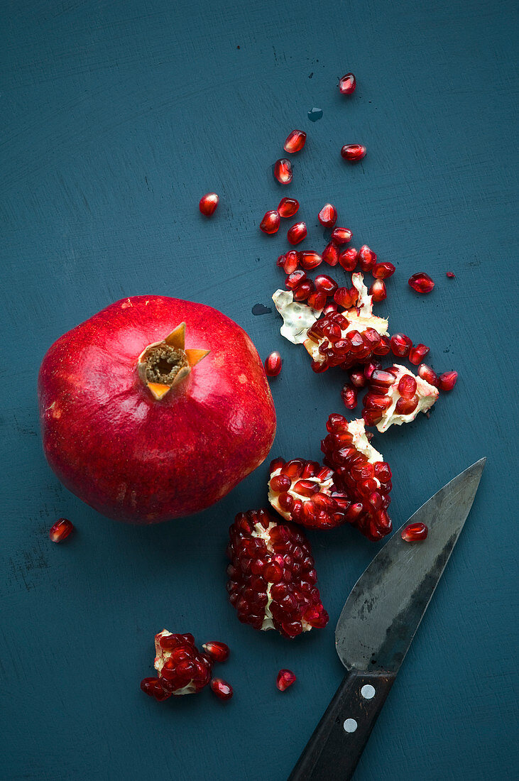 A whole pomegranate and pomegranate pieces with a knife on a blue background