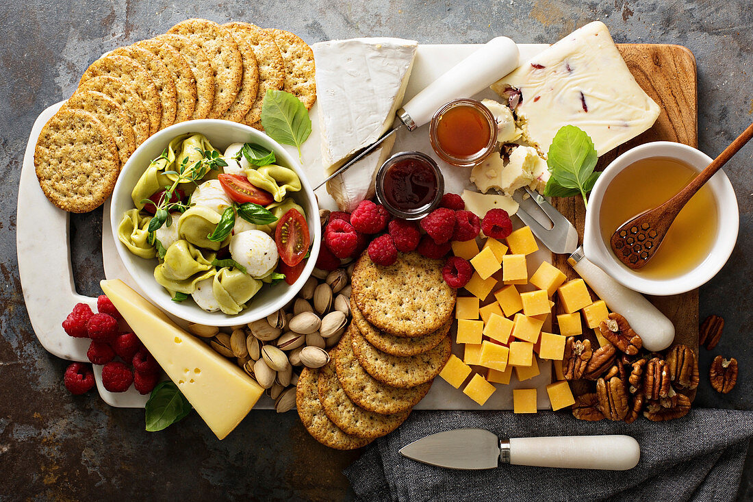 A cheese plate with tortellini salad, crackers, fruit and nuts