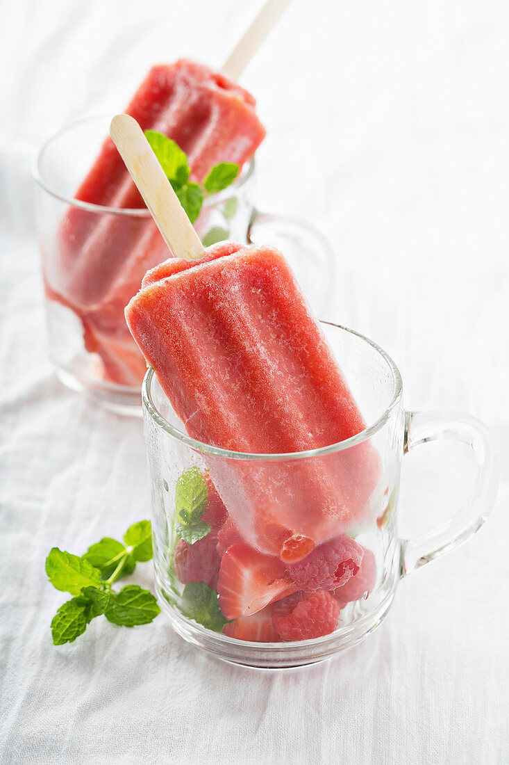Strawberry ice lollies served with berries in glass cups