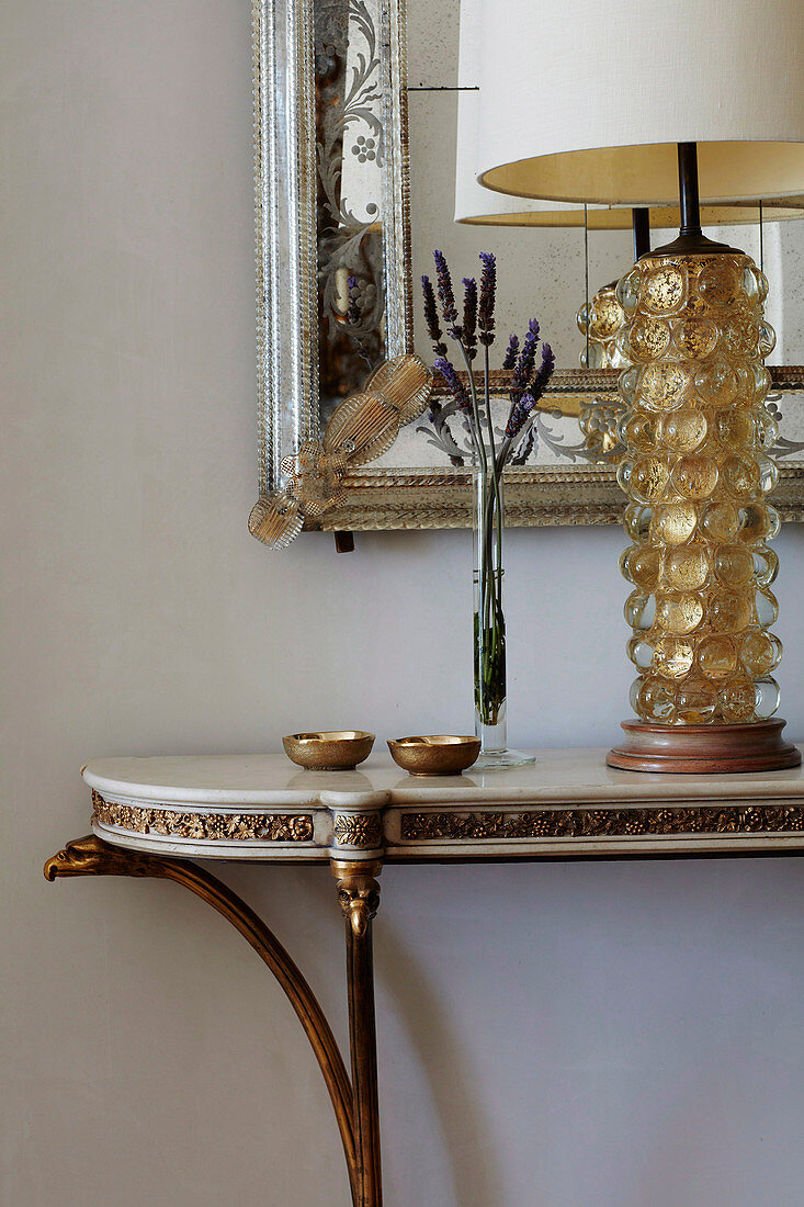 Elegant console with table lamp in front of wall mirror with silver frame