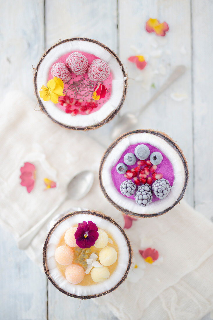 Angefrorene Smoothie-Bowls mit Früchten und Essblüten in Kokosnusschalen