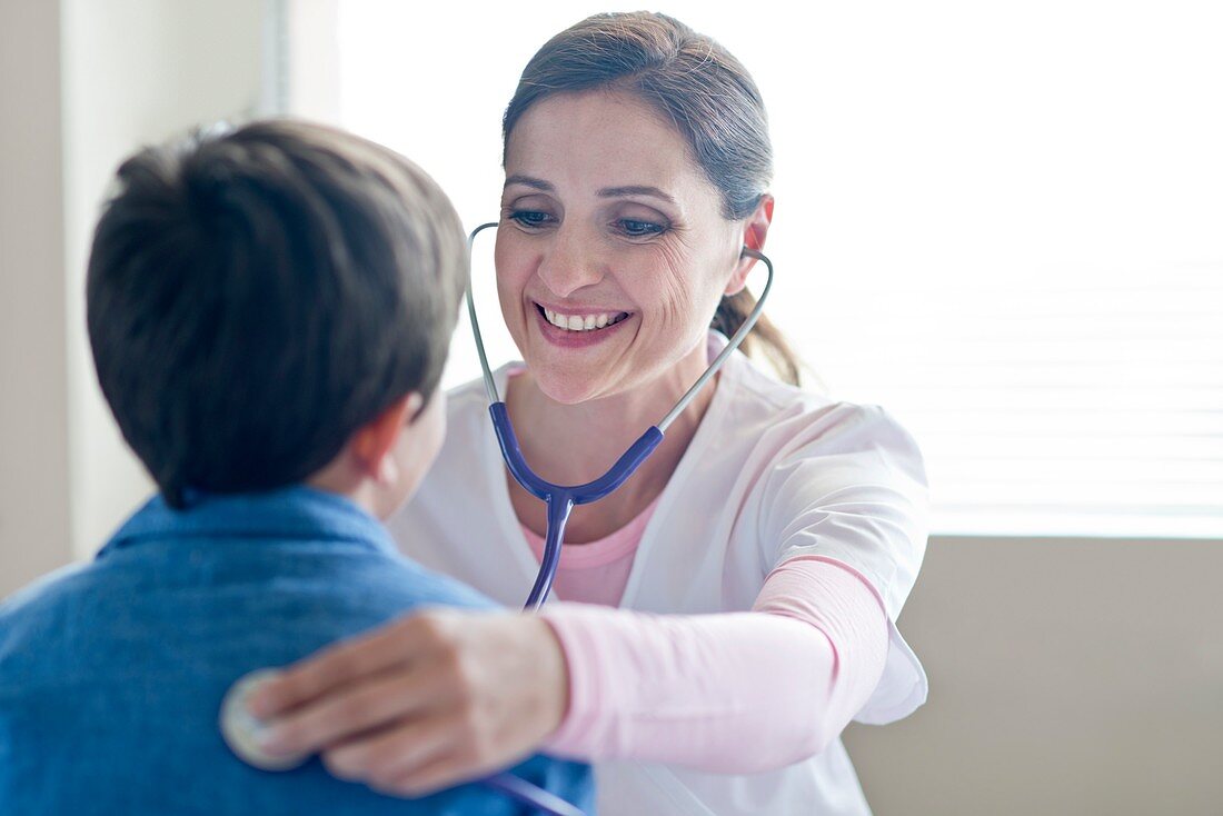 Nurse using stethoscope, smiling toward boy