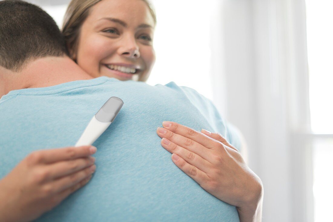 Woman hugging man and holding pregnancy test