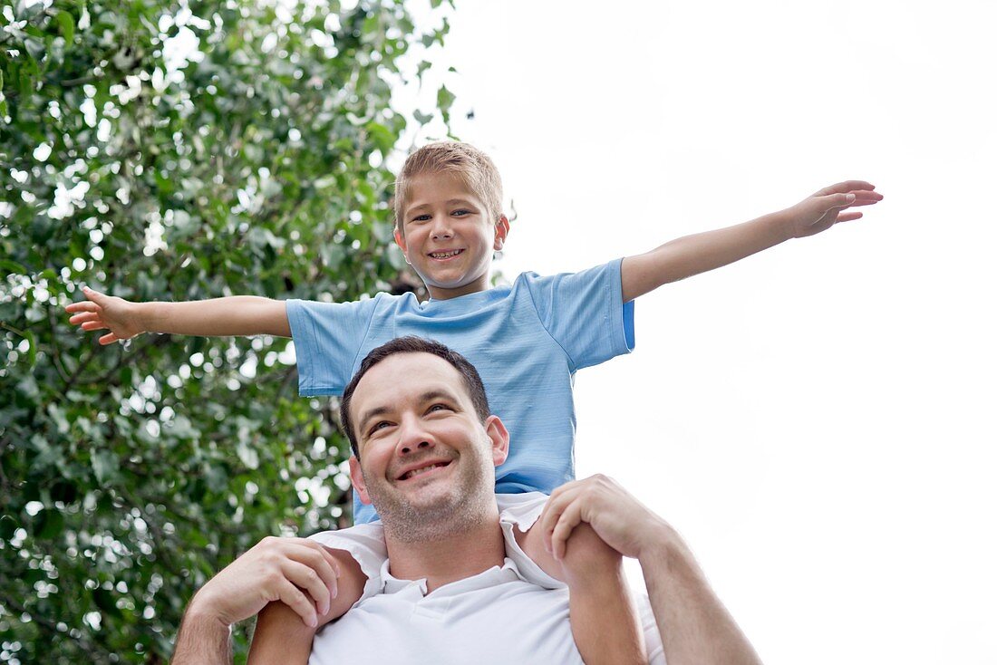 Father carrying son on shoulders with arms out