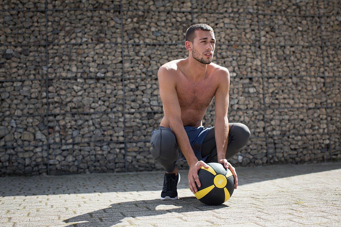 Young man crouching with medicine ball