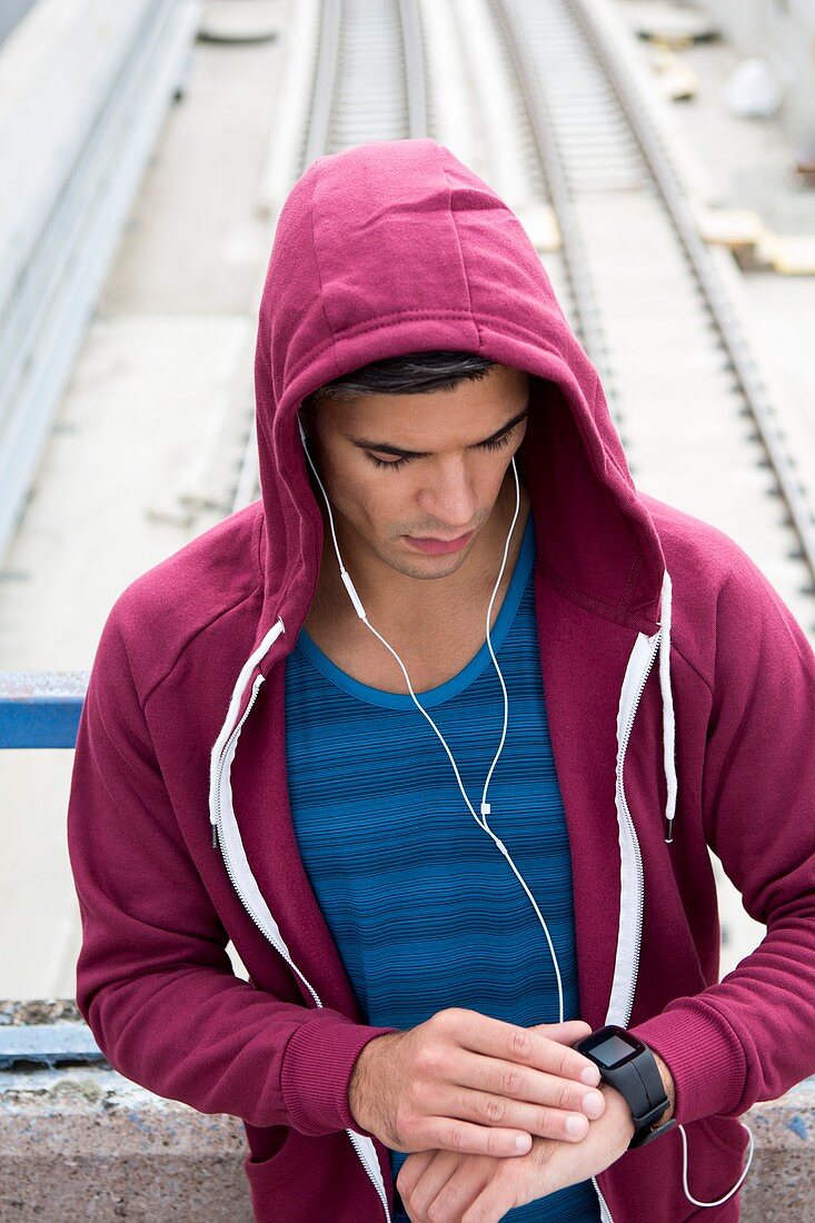 Young man wearing ear phones checking watch