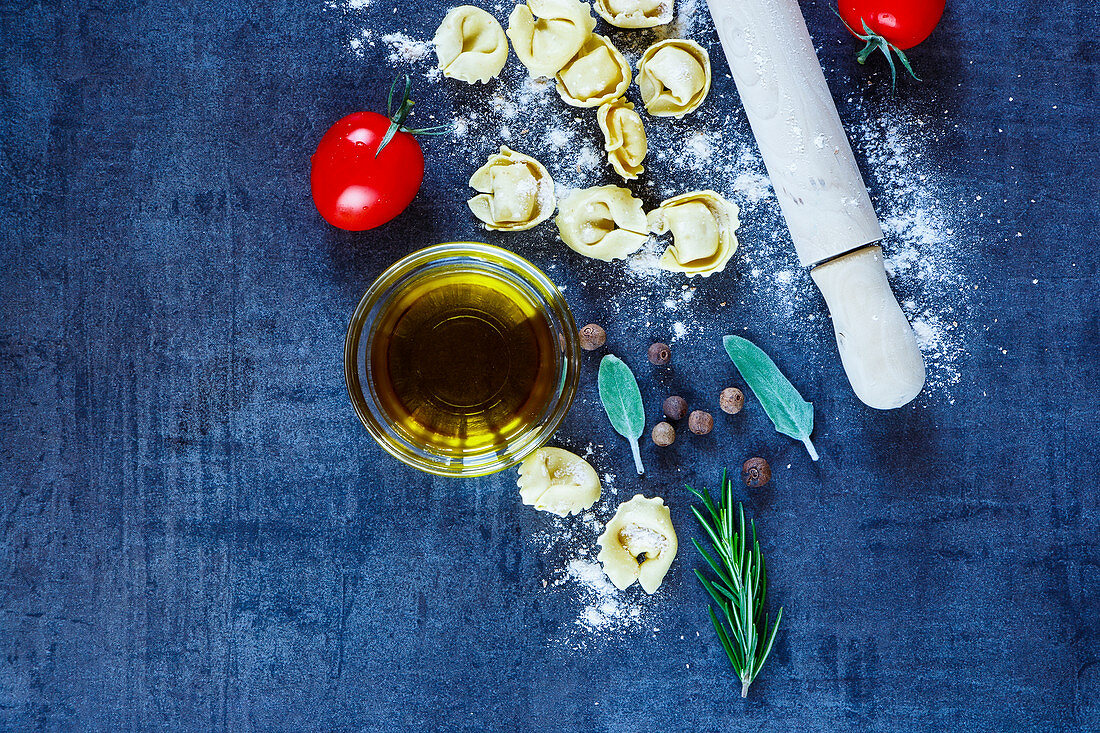 Selbst gemachte, italienische Tortellini, Tomaten, Olivenöl und Kräuter auf blauem Untergrund