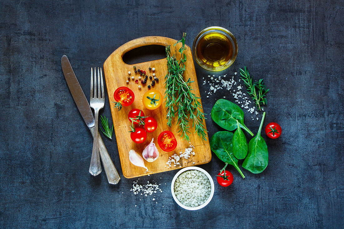 Tasty vegetarian ingredients, olive oil and seasoning on rustic wooden cutting board over dark vintage background