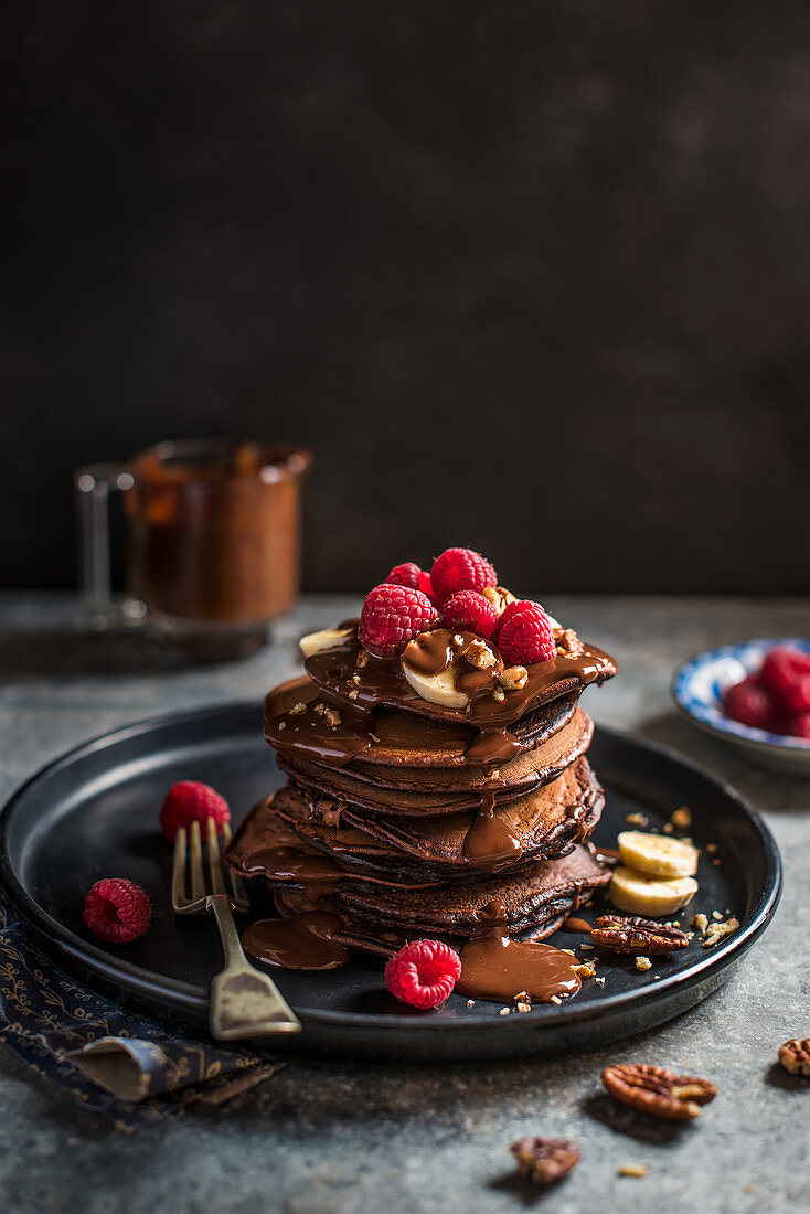Chocolate pancakes with chocolate sauce, sliced bananas ad raspberries
