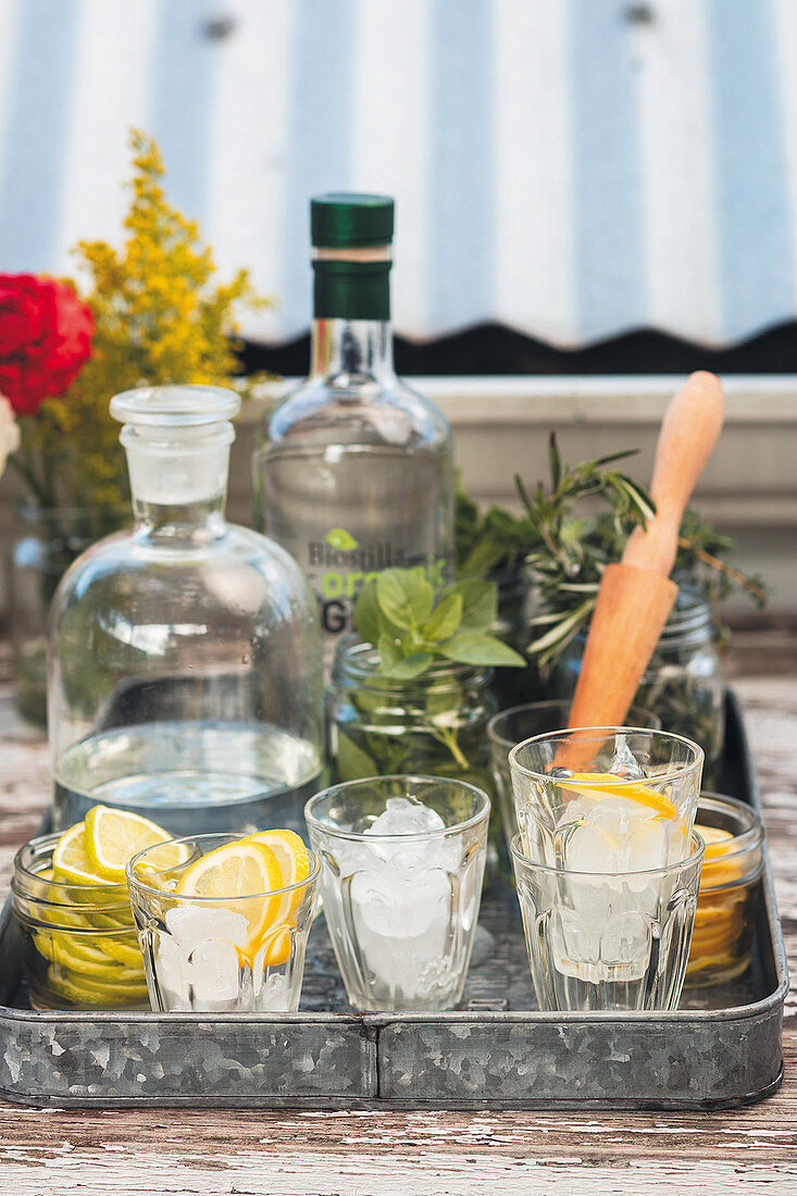 Vorbereitete Gläser mit Eiswürfeln und Zitronenscheiben, Wasserflaschen und Kräuter