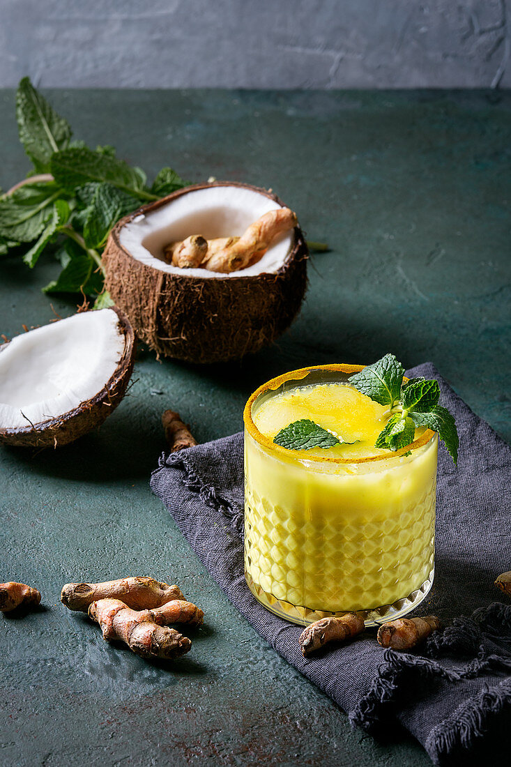 Glass of ayurvedic drink golden coconut milk turmeric iced latte with curcuma powder, mint and ingredients