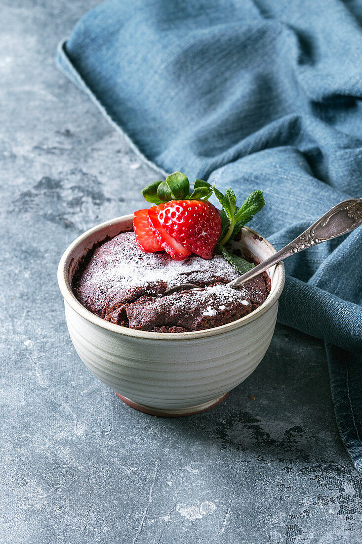 Chocolate mug cakes from microwave with strawberry and sugar powder over blue texture background