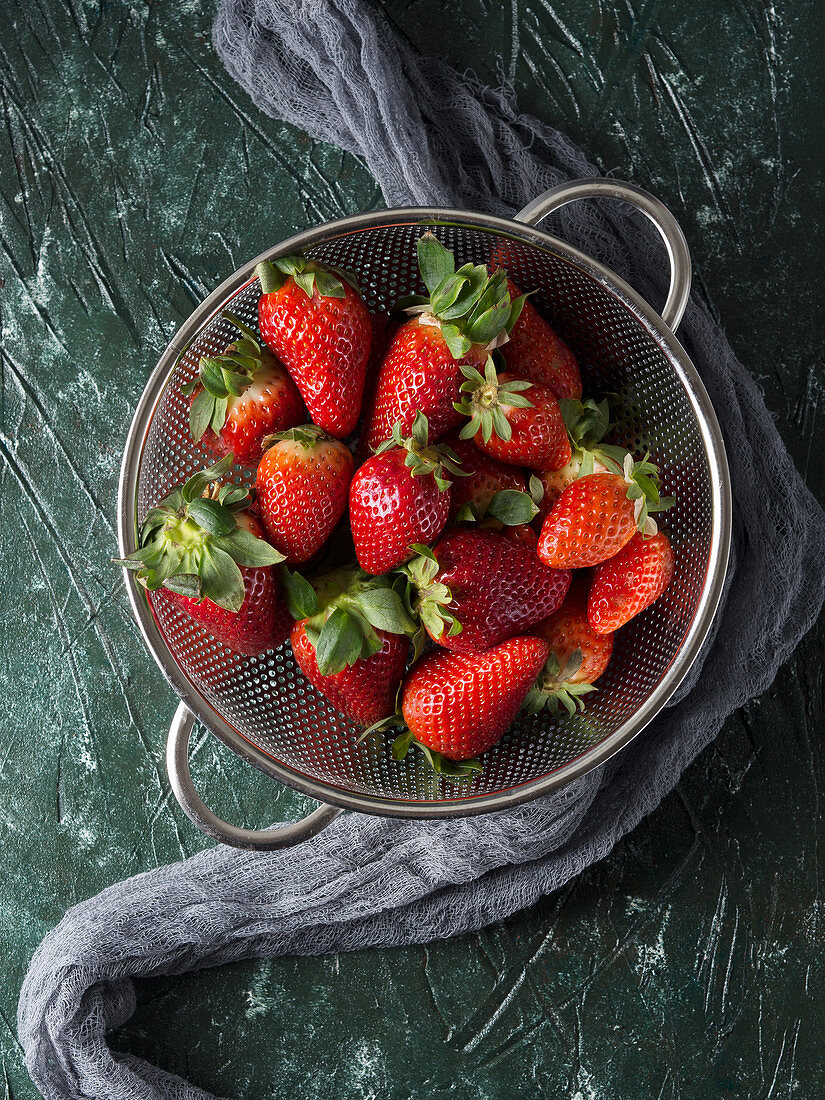 Fresh strawberries in a metal colander over green background