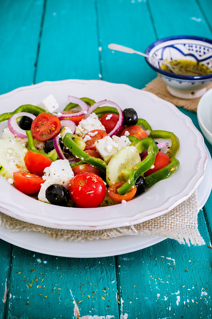 Griechischer Salat in weißem Teller auf türkisfarbenem Tisch