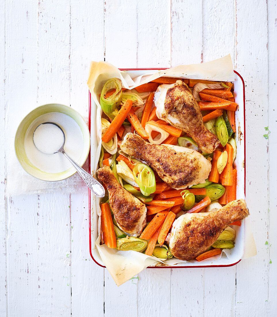 Chicken legs, carrots and leek on a baking tray