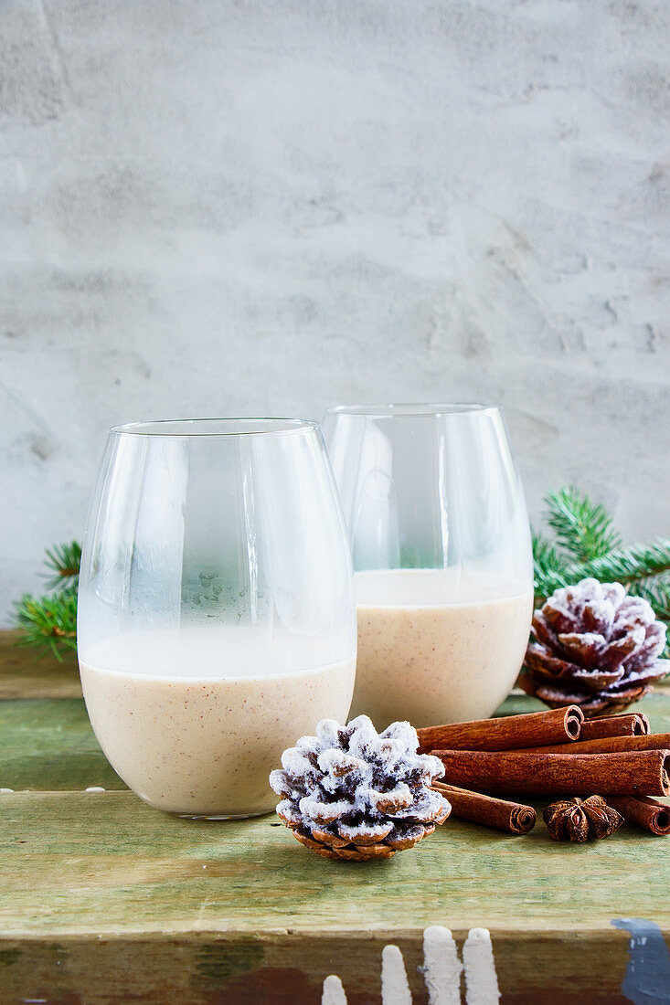 Glasses of Traditional winter eggnog with milk, rum and cinnamon, christmas decorations on wooden table