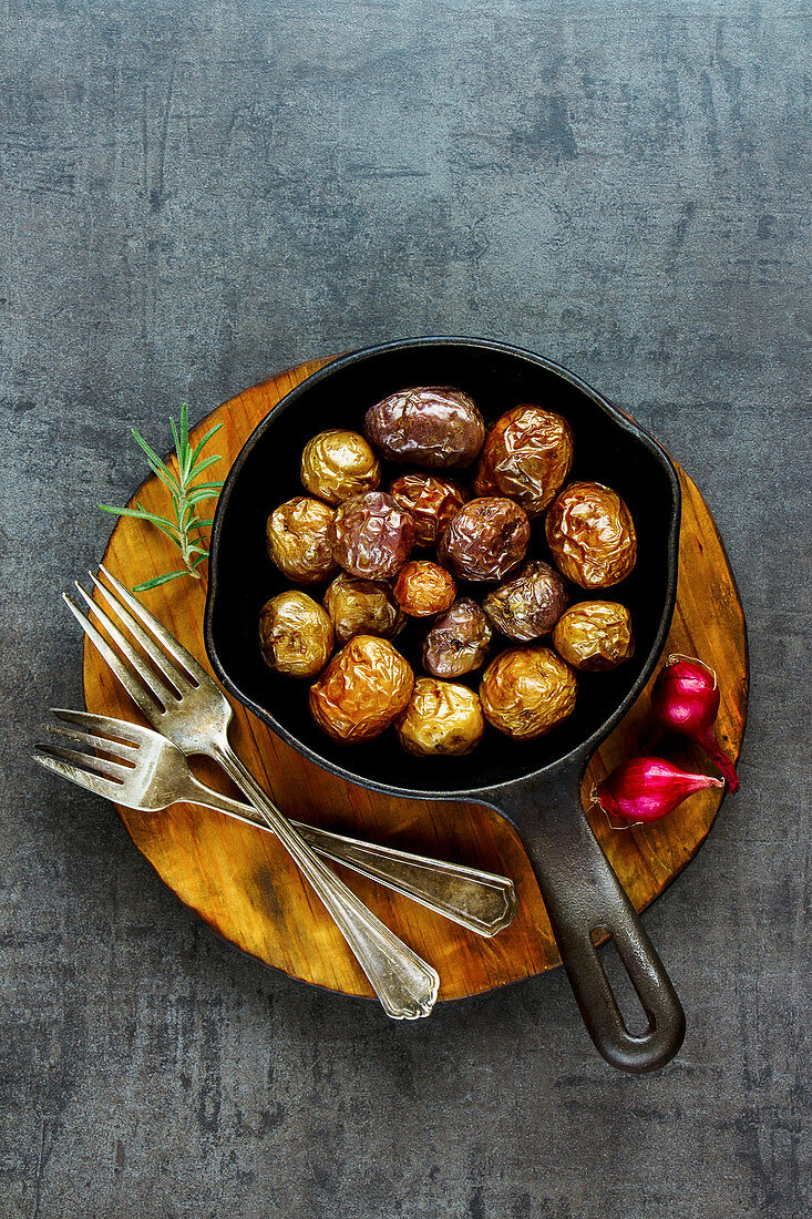Tasty fried baby potatoes in vintage cast iron pan on wooden board over black concrete background