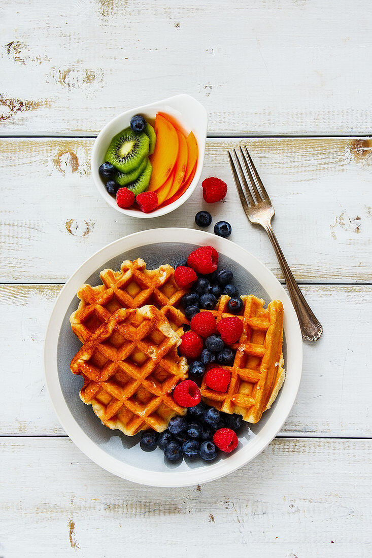 Delicious breakfast set. Warm homemade traditional belgian waffles with fresh berry and fruit on white rustic wooden background