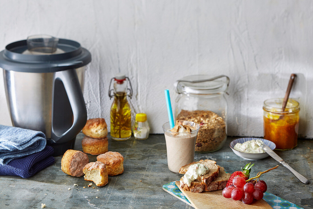 Stillleben mit Brötchen, Smoothie, Müsli, Brot, Aufstrichen, Obst und Küchenmaschine