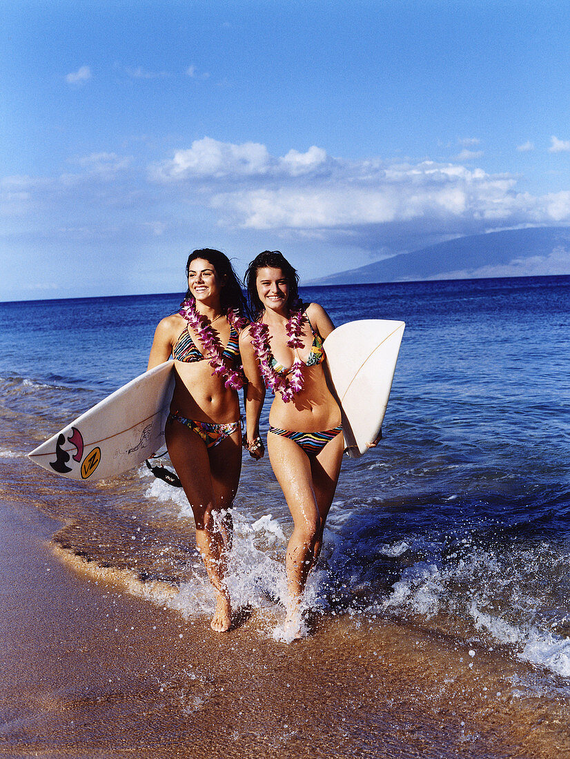Zwei junge Frauen mit Surfbrettern im Bikini am Strand