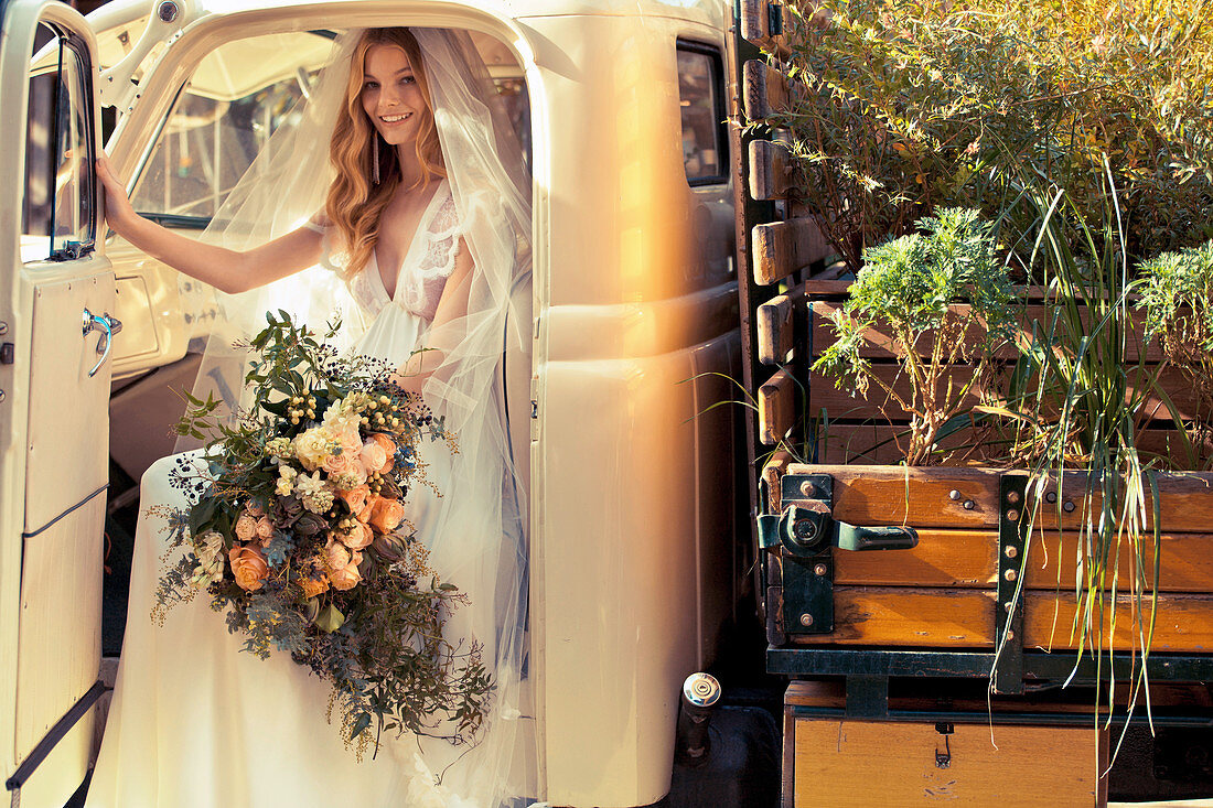 A bride wearing a white wedding dress with a lavish bouquet sitting in a pickup