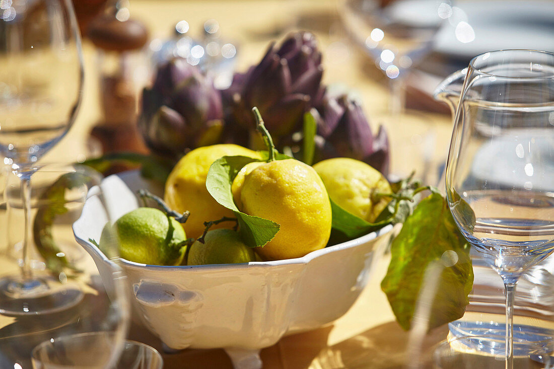 Frische Zitronen und Artischocken in Schale auf gedecktem Tisch im Freien