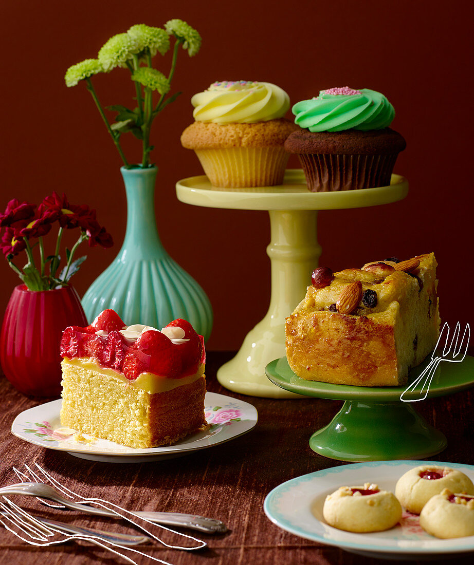 Sponge cake with vanilla pudding and fruit, cupcakes, shortbread jam biscuits, and raisin and almond spiral cake