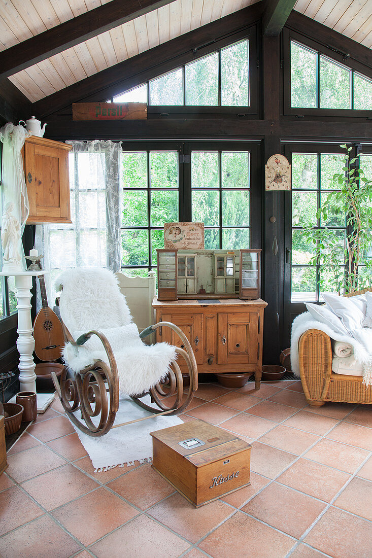 Fur blanket on old rocking chair next to wooden cabinet in conservatory