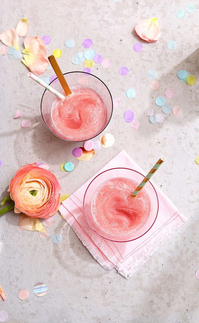 Two glasses of Frosé, a buttercup flower and confetti on a concrete surface