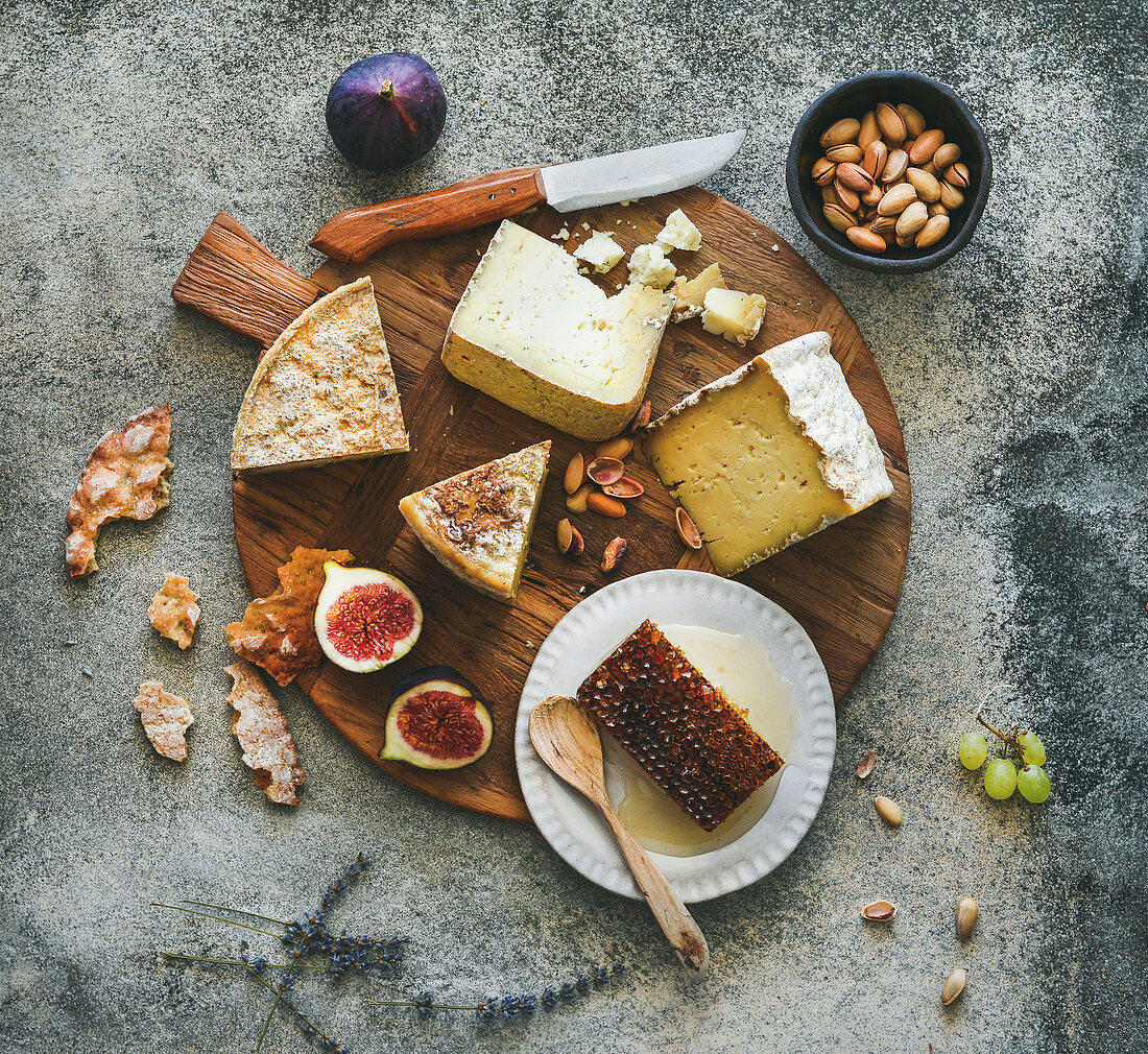 Flat-lay of cheese platter with cheese assortment, figs, honey and nuts over grey concrete background