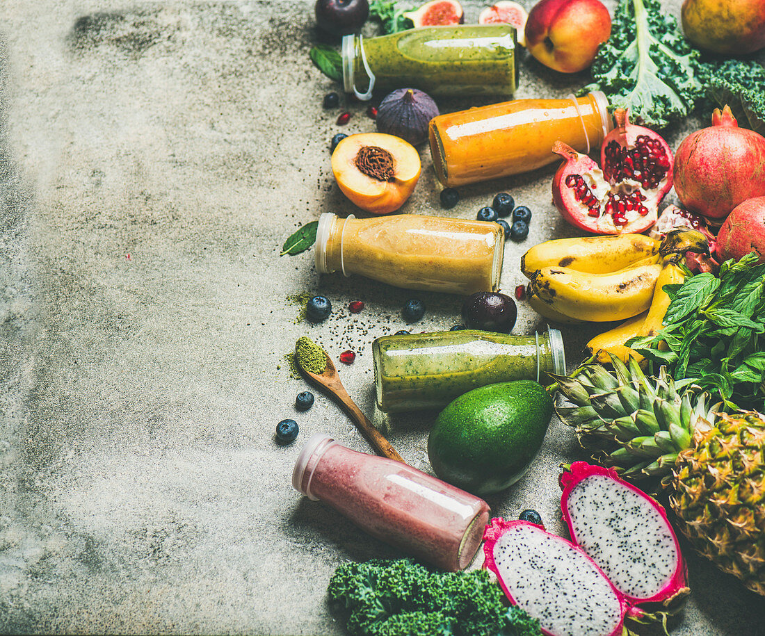 Verschiedene Smoothies in Flaschen umgeben von tropischen Früchten und Superfoods