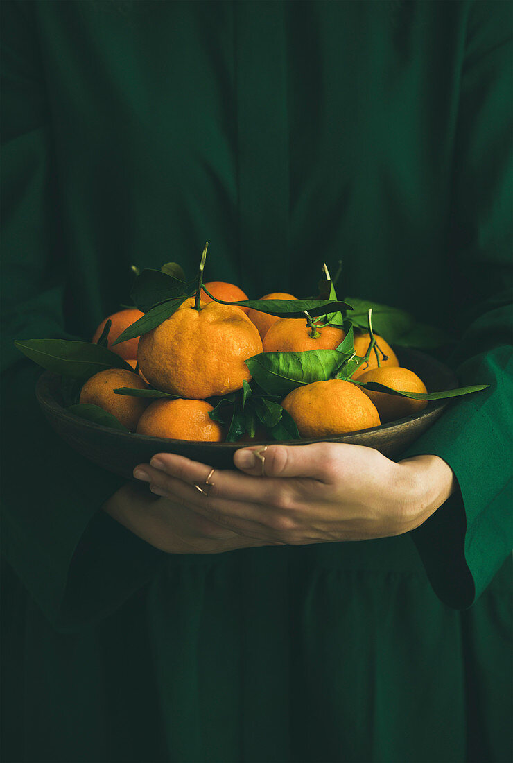 Junge Frau im grünen Kleid hält Schale mit frischen Mandarinen in den Händen