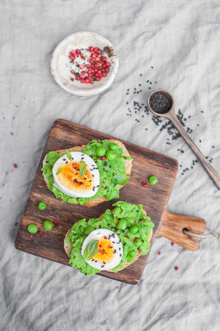 Toasts with mashed green peas and boiled egg, served with pink pepper and black sesame