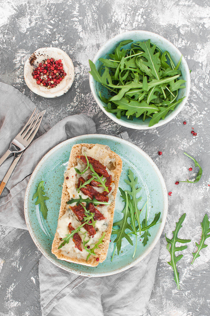 Gorgonzola toast with sun dried tomatoes, served with arugula and pink pepper