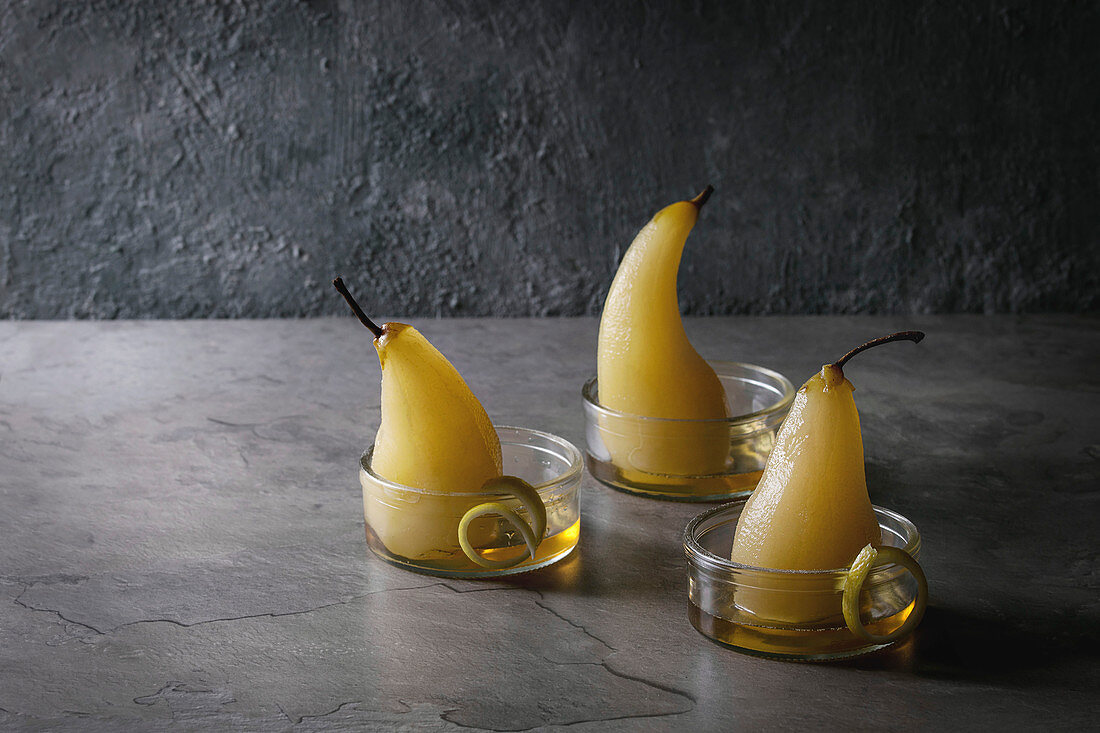 Traditional dessert poached pears in white wine served in glass bowls with syrup and lemon zest