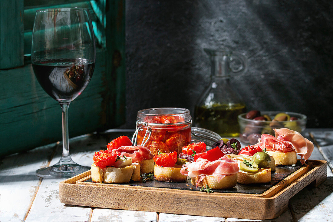 Verschiedene Bruschetta mit Schinken, Tomaten und Oliven auf Holzplatte