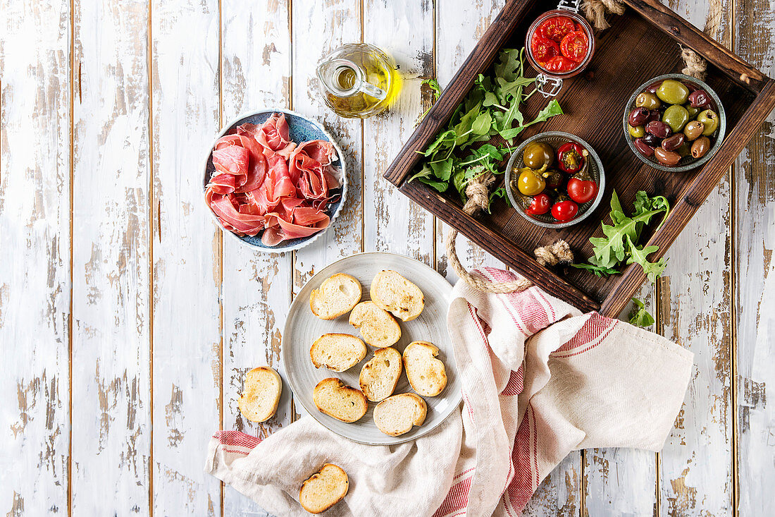 Zutaten für verschiedene Bruschetta mit Schinken, Tomaten und Oliven (Aufsicht)