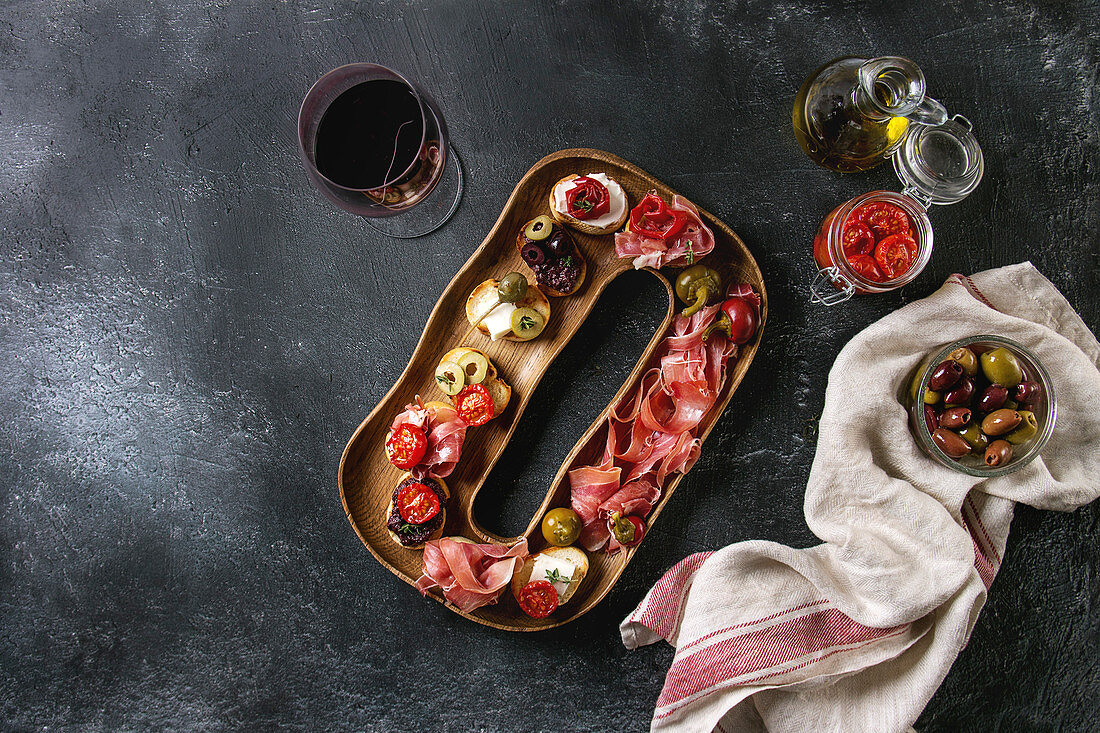 Tapas or bruschetta variety: Bread with ham prosciutto, sun dried tomatoes, olive oil, olives, pepper on decorative wood plate