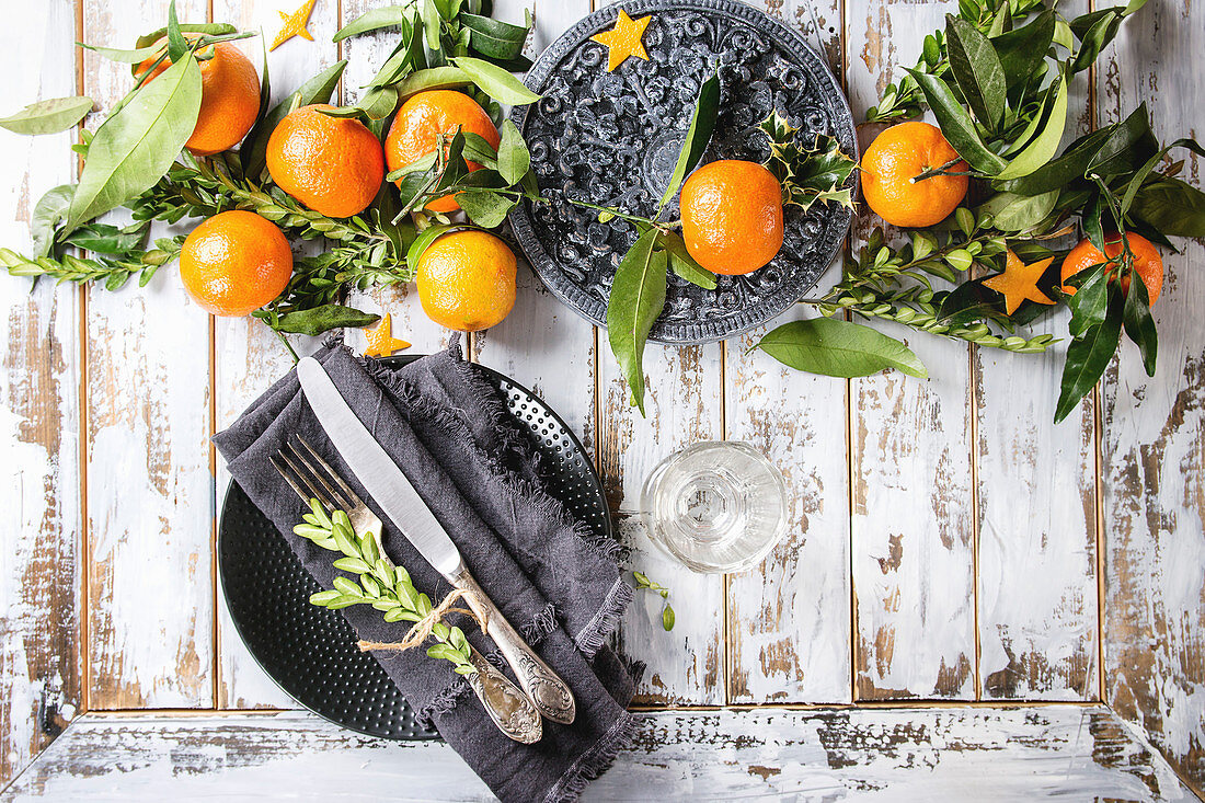 Christmas table decorations with clementines or tangerines with leaves and green branches on black ornate board