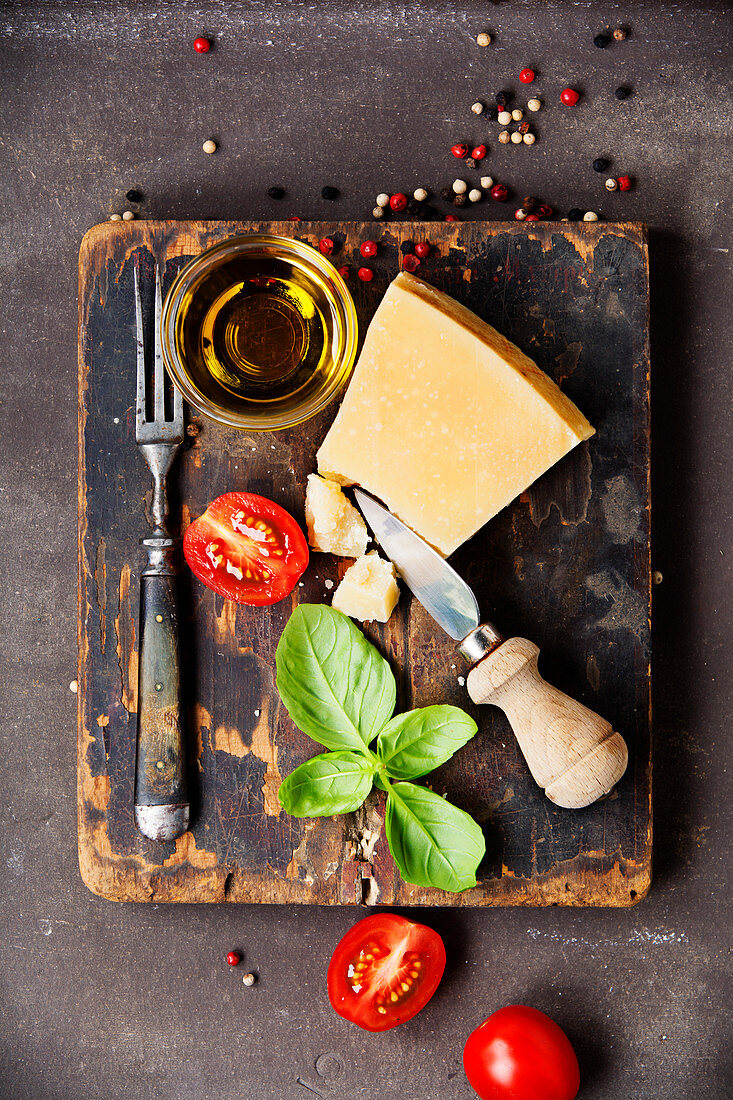 Fresh food ingredients for italian cuisine (Parmigiano, tomato, basil, olive oil) on rustic background