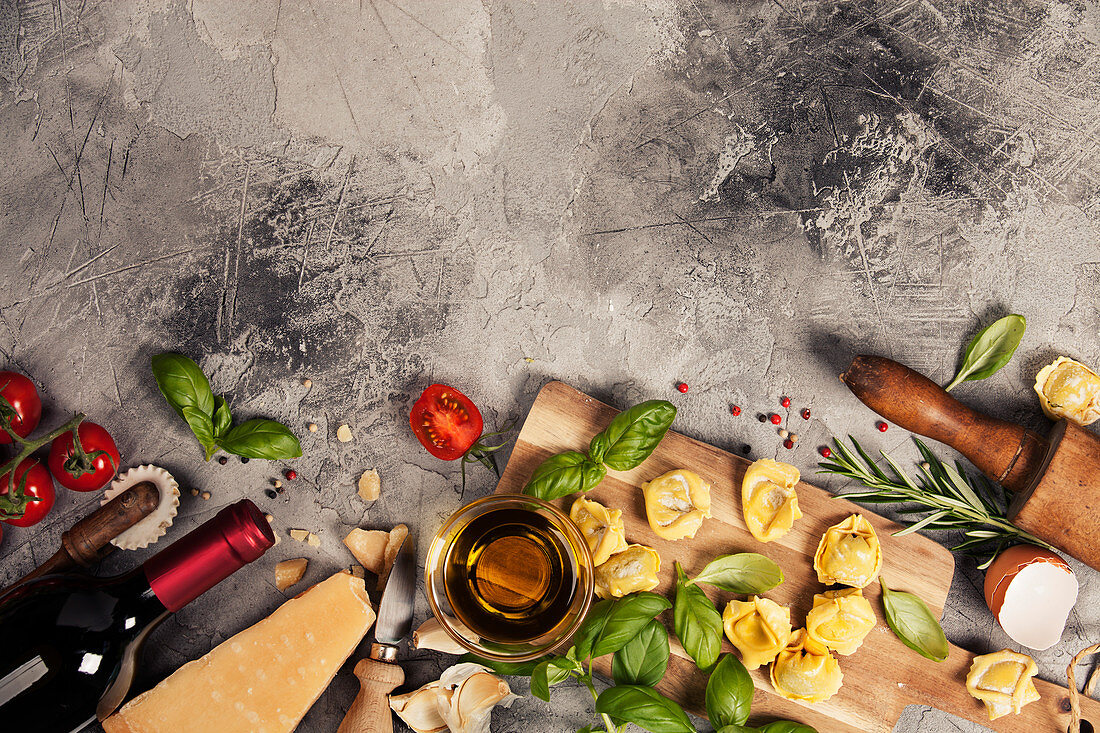 Italian food background with ravioli, vine tomatoes, basil, spaghetti, spinach, onion, parmesan, olive oil, garlic, peppercorns, rosemary and wine
