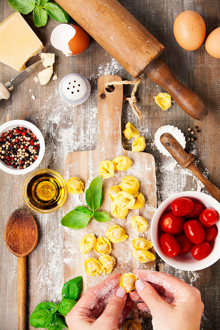 Raw italian pasta tortellini with ingredients on wooden board