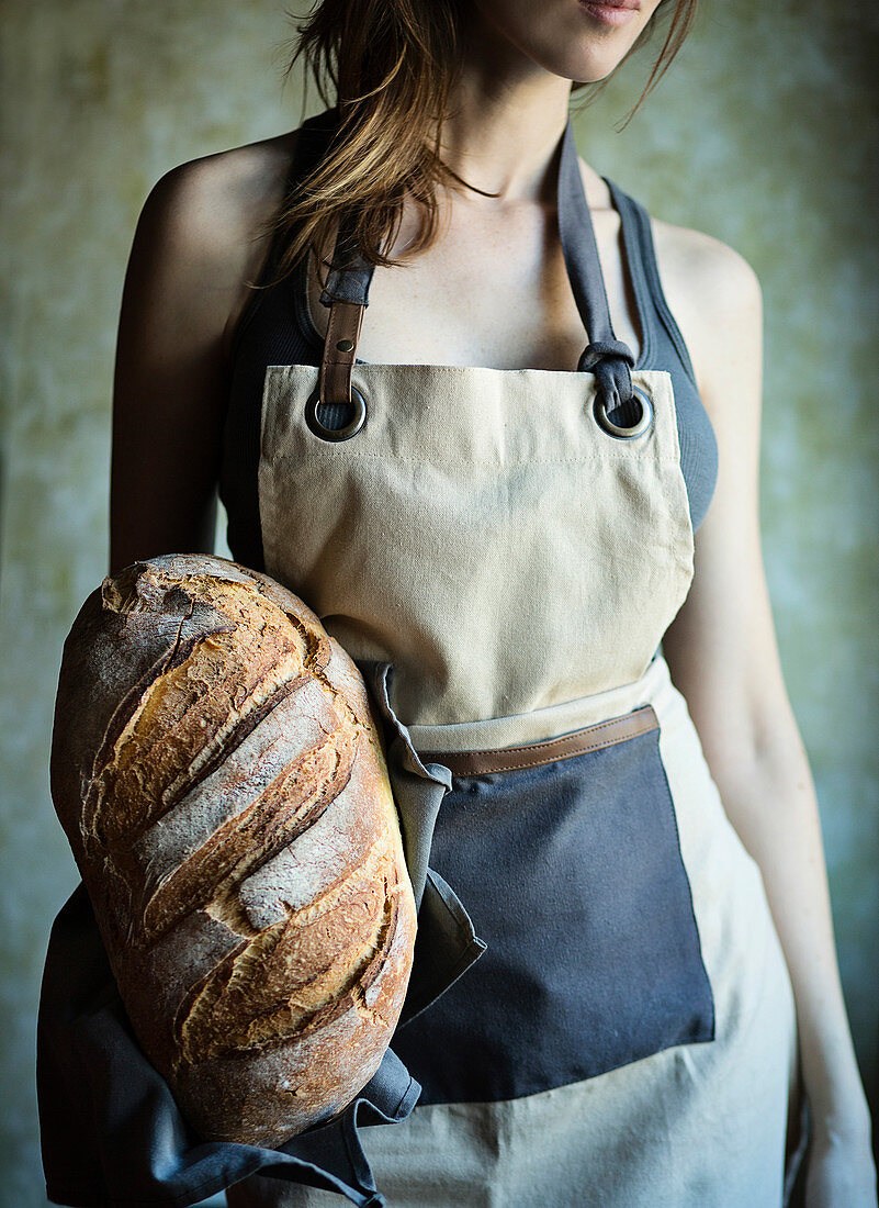 Junge Frau mit Schürze hält frischen italienischen Brotlaib in der Hand