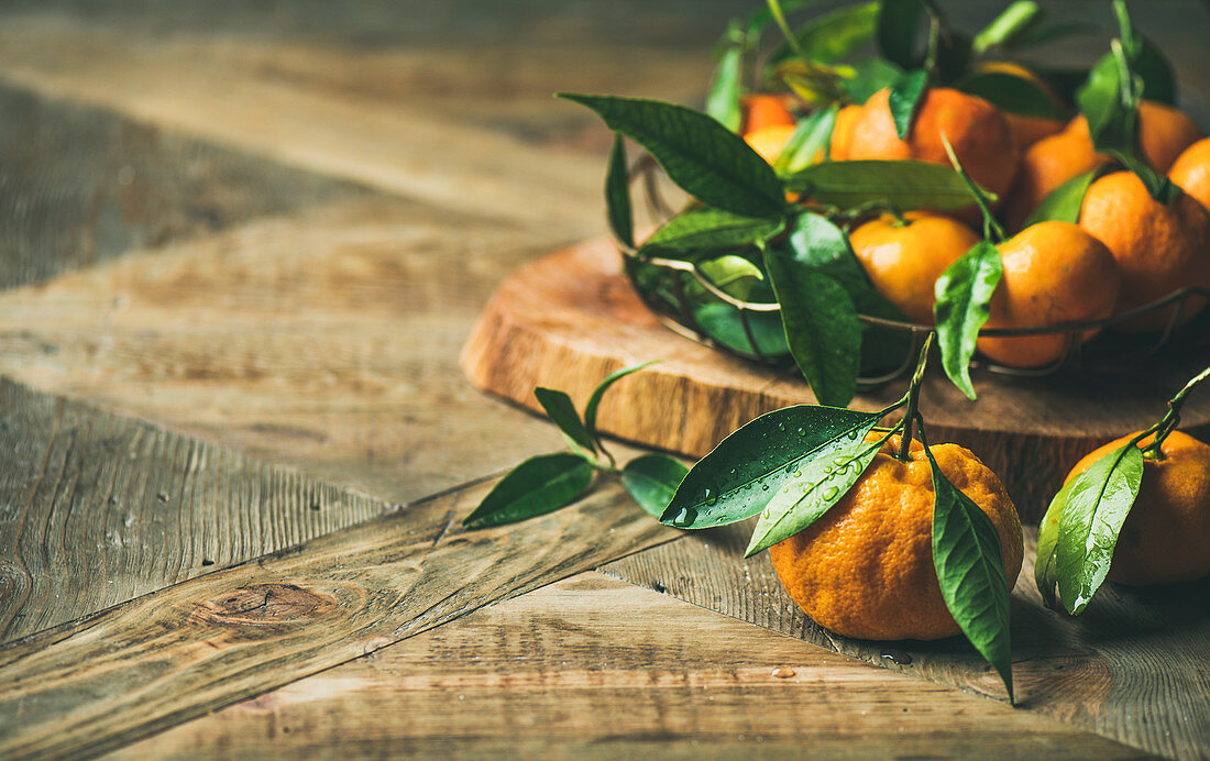 Fresh tangerines with leaves on board over rustic wooden table background