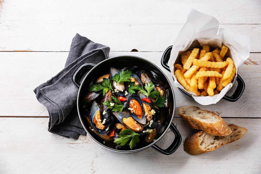 Shellfish Mussels Clams in black cooking dish pan and French Fries on white wooden background